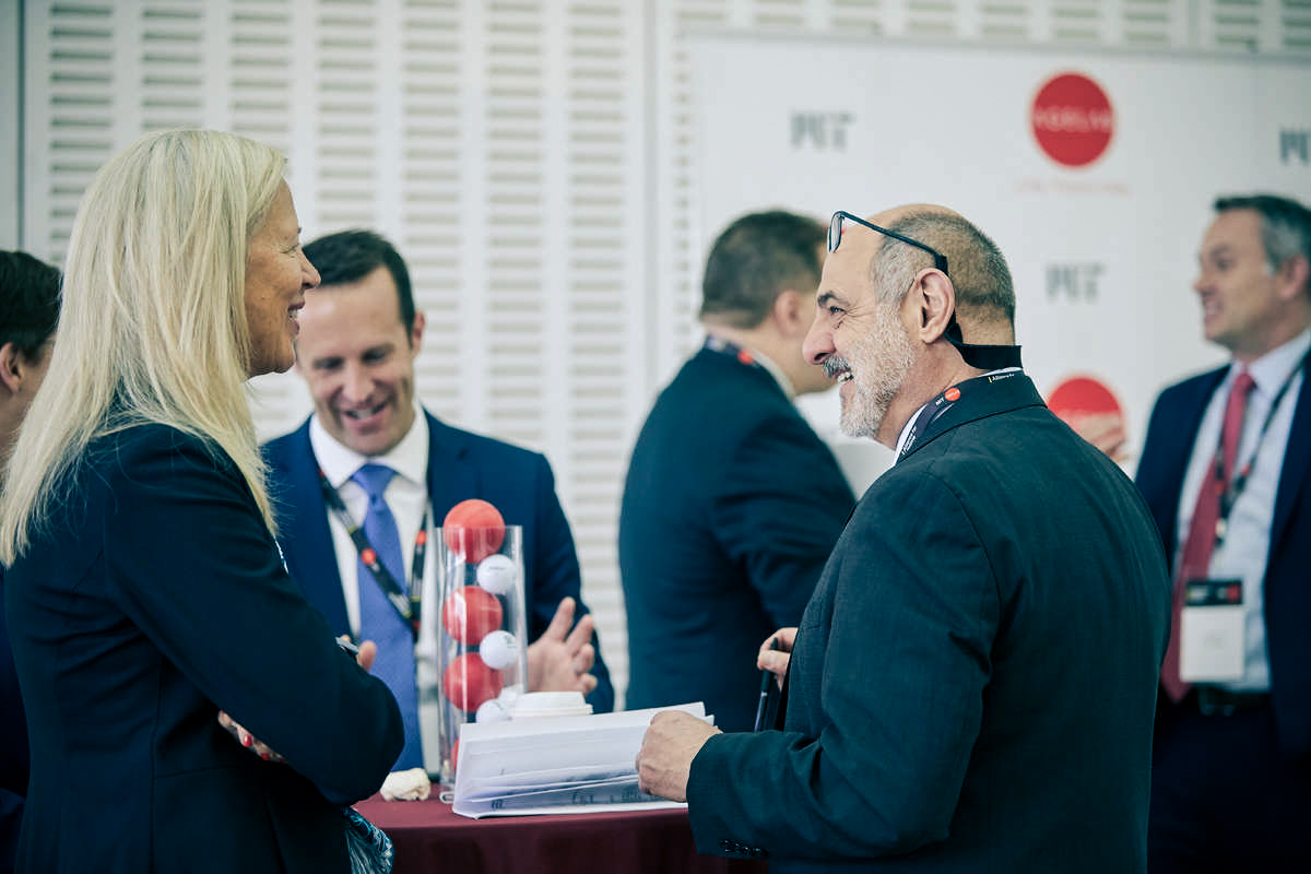 Woman and man stand near a table smiling, with other people in the background.